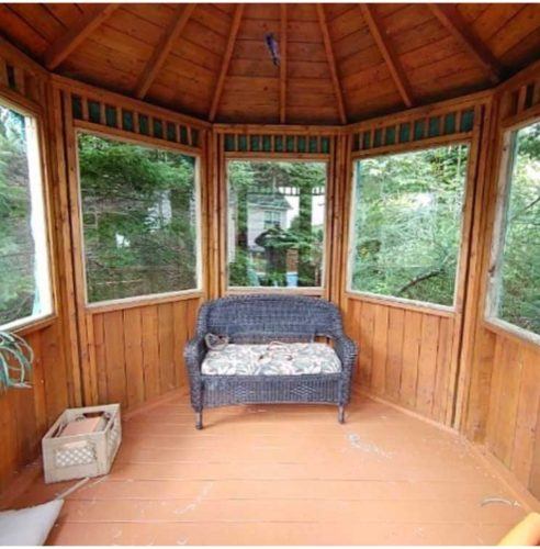 inside of a wooden gazebo with glass windows and a grey couch in the middle